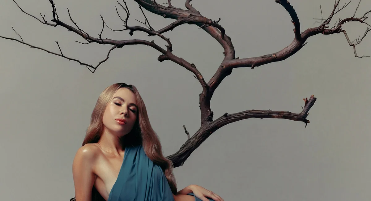 WHIPPED CREAM in a blue-dress studio portrait beside a bare tree, from her HOME WAS ALWAYS ME press shoot