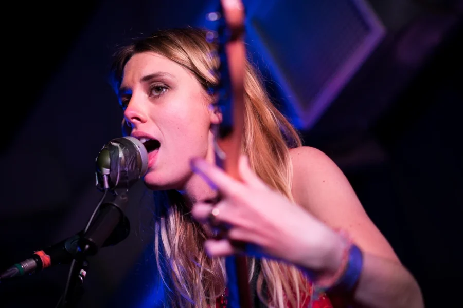 Ellie Rowsell of Wolf Alice singing into a microphone under blue stage light