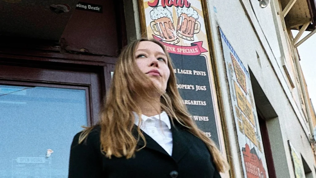 Julia Jacklin standing outside a pub beneath a happy hour sign