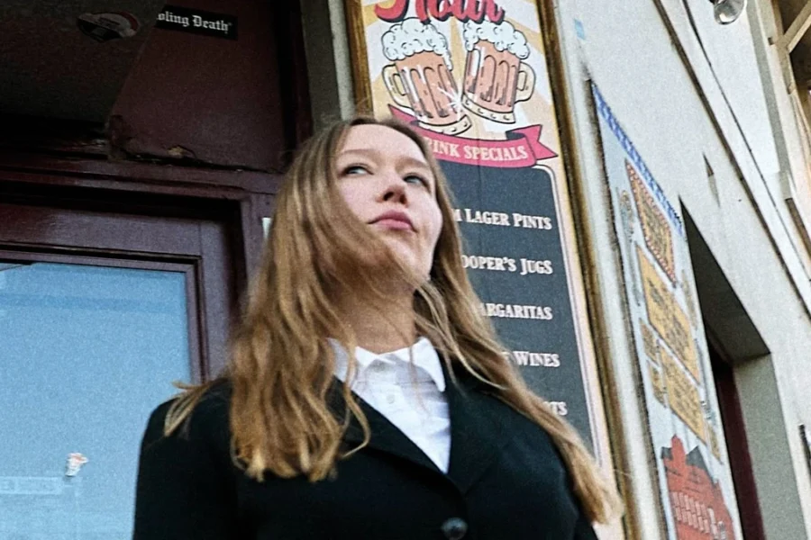 Julia Jacklin standing outside a pub beneath a happy hour sign